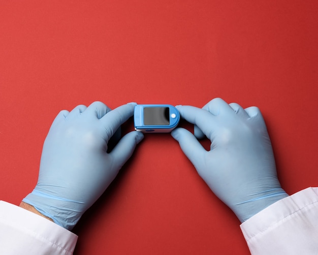 Oxymètre de pouls électronique entre les mains d'un médecin, portant des gants en latex bleu, vue du dessus