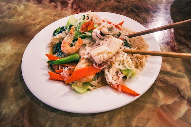 Pad de fruits de mer Plat thaï de nouilles de riz frites thaïlandaises sur une plaque blanche avec des baguettes et une garniture de carottes râpées