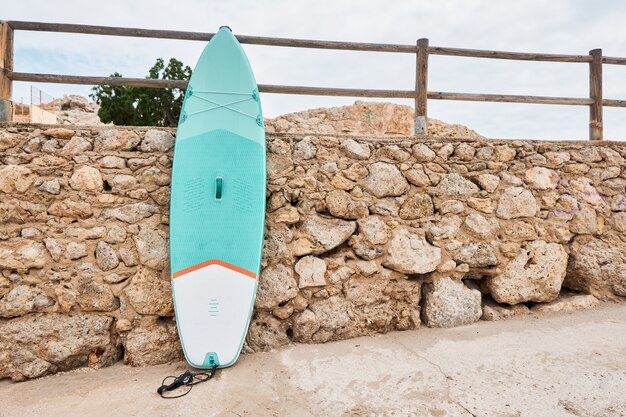 Photo paddle board appuyé contre un mur de pierre sur la plage