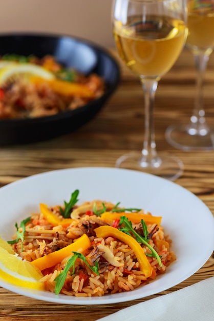 Paella aux fruits de mer, légumes, herbes et vin blanc sur une table en bois.