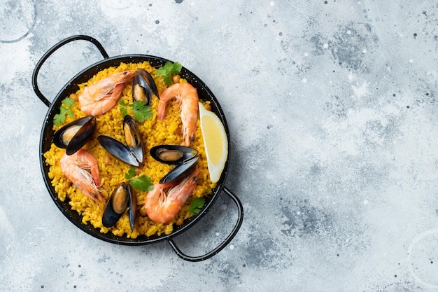 Paella de fruits de mer espagnole traditionnelle dans une poêle avec pois chiches crevettes moules calamars sur fond de béton gris clair Vue de dessus avec espace de copie