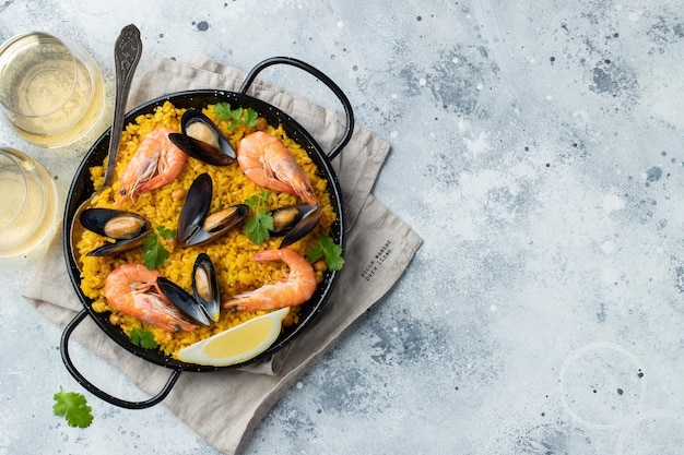 Paella traditionnelle espagnole aux fruits de mer dans une casserole avec des pois chiches, des crevettes, des moules, des calmars sur un fond de béton gris clair Vue supérieure avec espace de copie