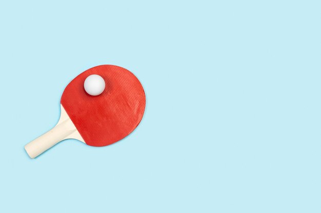 Pagaie de ping-pong rouge et une boule blanche sur un bleu clair