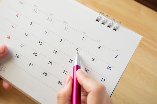 Page de calendrier avec une main féminine tenant un stylo sur la table de bureau