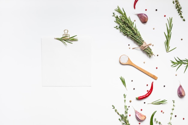 Page de papier de recette vierge avec vue aérienne à plat avec carte d'invitation à l'espace de texte de maquette de clip sur fond blanc avec des herbes vertes et des épices. Conception de blog de cuisine de livre de recettes de menu avec des ingrédients de cuisine