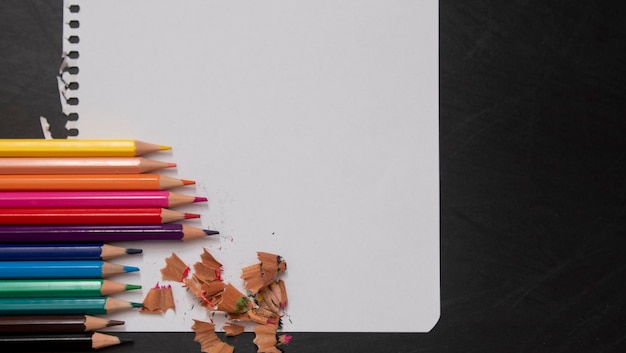 Page vierge d'un cahier sous forme de maquette à côté de crayons de différentes couleurs sur un fond de tableau noir