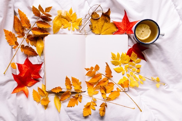 Photo des pages de bloc-notes dans un espace confortable avec une tasse d'émail de thé au gingembre au citron et des feuilles d'automne colorées