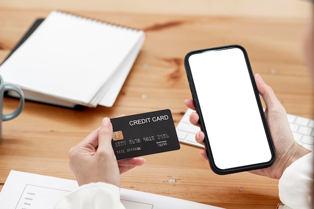 Paiement en ligne, mains de femme tenant une carte de crédit et utilisant un téléphone intelligent pour faire des achats en ligne. Maquette smartphone à écran blanc pour l'affichage du produit.