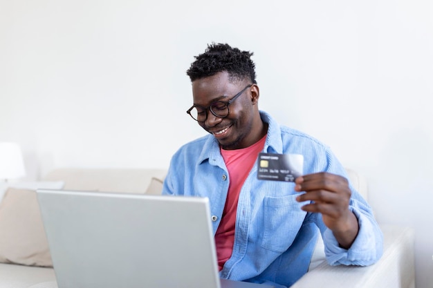 Paiement en ligneJeune homme tenant une carte de crédit et un ordinateur portable pour faire des achats en ligne concept de vendredi noir ou cyber lundi Homme payant avec carte de crédit sur ordinateur portable au bureau à domicile