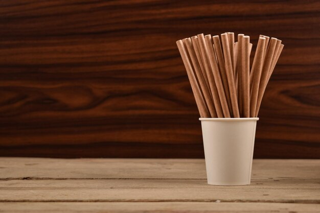 Pailles en papier dans un gobelet en papier sur une table en bois