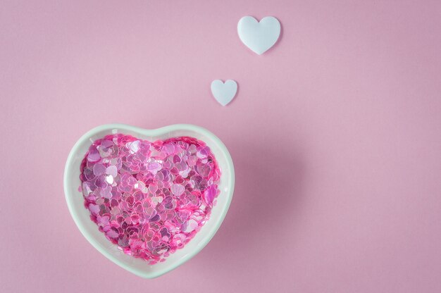 Paillettes dans un bol en forme de coeur avec des coeurs en papier