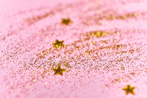 Paillettes de paillettes dorées et étoiles sur une surface rose