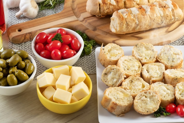 Pain à l'ail dans une assiette carrée blanche sur la table avec du fromage, du romarin, des olives et des tomates cerises.