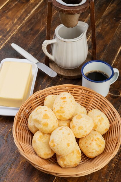 Pain au fromage brésilien typique dans un panier avec du café sur une table en bois.