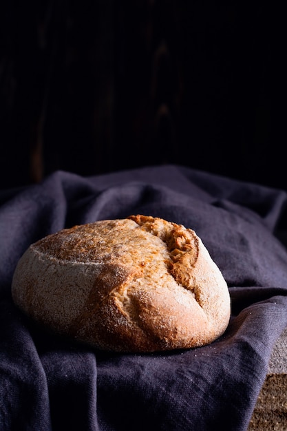 Pain au levain fait maison fraîchement cuit sur une serviette en lin foncé, fond en bois.