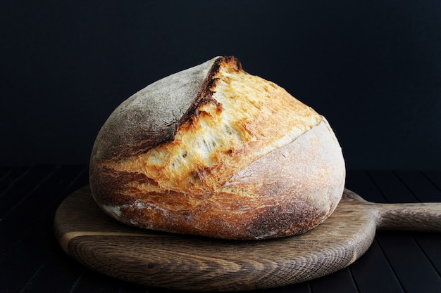 Pain au levain sur planche coupée en bois sur fond noir photographie alimentaire pain fait maison