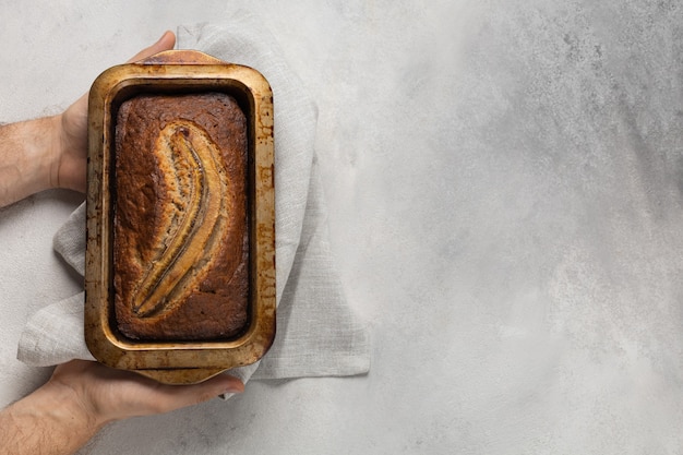 Pain aux bananes prêt dans un plat de cuisson rectangulaire dans les mains masculines du boulanger sur fond clair