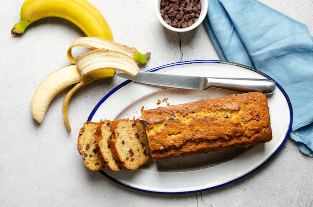 Un pain aux bananes en tranches avec des pépites de chocolat avec une serviette bleue sur fond gris.