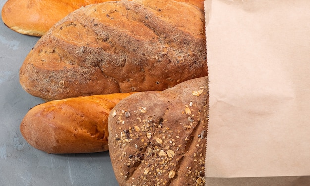 Pain et baguette fraîchement cuits dans un sac en papier sur un fond texturé gris.