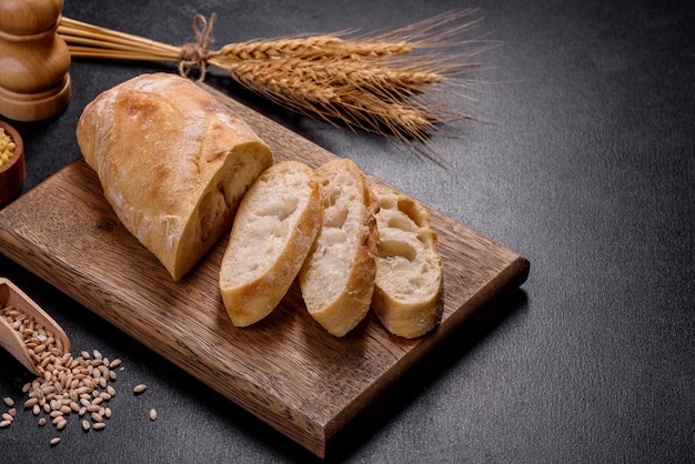 Pain baguette français tranché sur une planche à découper en bois sur un fond de béton foncé