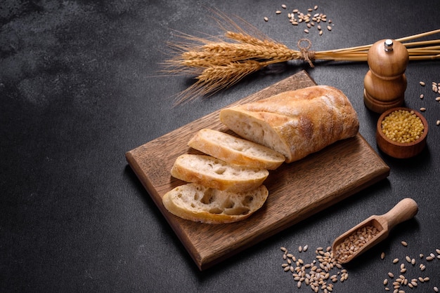 Pain baguette français tranché sur une planche à découper en bois sur un fond de béton foncé