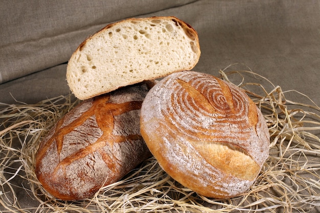 Pain blanc deux formes différentes se trouvant dans la paille sur une nappe en lin gris