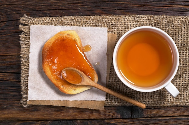 Pain blanc rôti avec de la confiture d'abricot et une tasse de thé sur une table en bois rustique. Vue d'en-haut