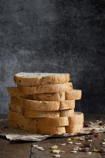 Pain de blé entier à grains tranchés sur fond de bois rustique foncé, ingrédients bio, aliments sains.