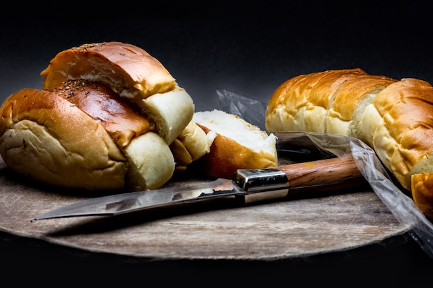 Pain de blé tranché au-dessus d'une planche à découper en bois avec un couteau sur un fond de texture rugueuse sombre