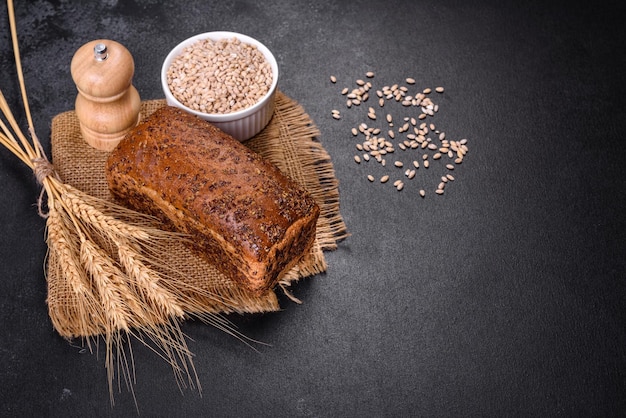 Pain brun frais cuit au four avec des oreilles et des grains de blé sur un fond de béton foncé