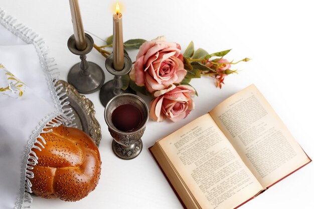 Pain challah recouvert d'une serviette spéciale vin de shabbat torah et bougies sur fond blanc Rituel de Shabbat juif traditionnel Shabbat Shalom