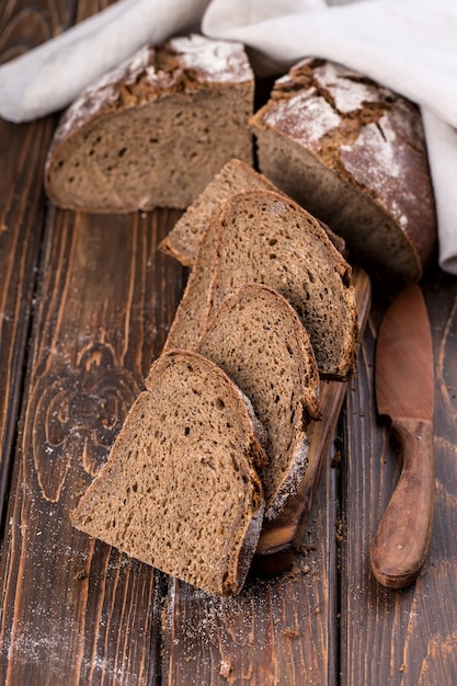 Pain chaud frais coupé en morceaux sur une vieille planche de bois, avec serviette, vertical