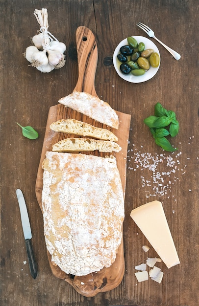 Pain ciabatta fraîchement cuit à l'ail, aux olives de la Méditerranée, au basilic et au parmesan sur un plateau de service sur une table en bois rustique