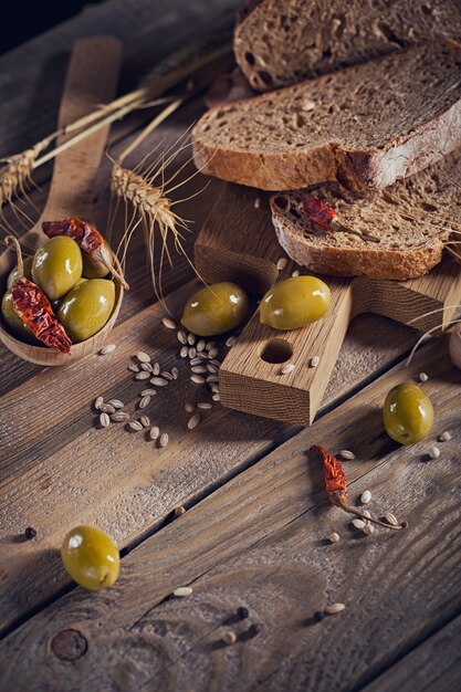 Pain croustillant multigrains frais, olives vertes, piment frais et épis de blé sur une table en bois rustique. Concept de magasin d'alimentation de boulangerie et d'épicerie.