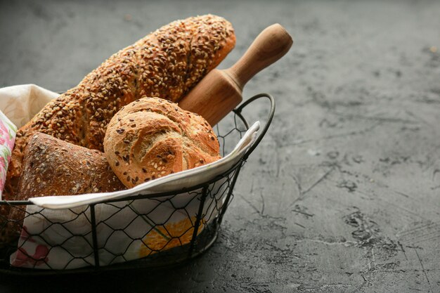 Pain dans un panier sur une surface noire. Pain assorti dans une corbeille en métal. Place pour la recette et le texte. Cuire le pain avec un rouleau à pâtisserie et de la farine. Pain de seigle, petits pains au sarrasin et baguette aux graines.