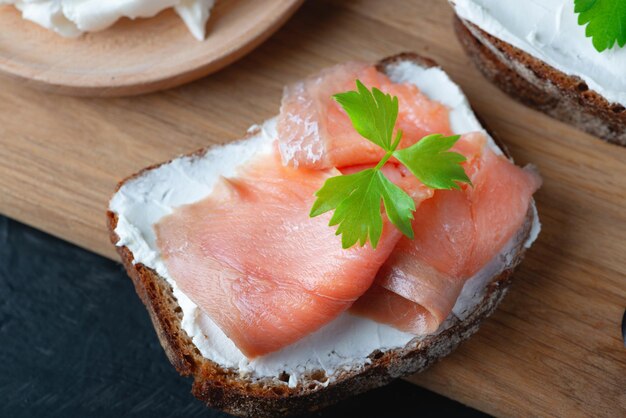 Pain fait maison sur une planche à découper en bois avec fromage blanc et saumon rose