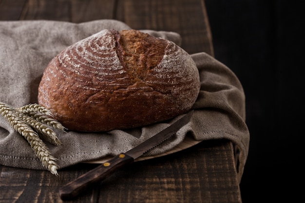 Pain fraîchement cuit au four avec un torchon et du blé sur une planche en bois foncé