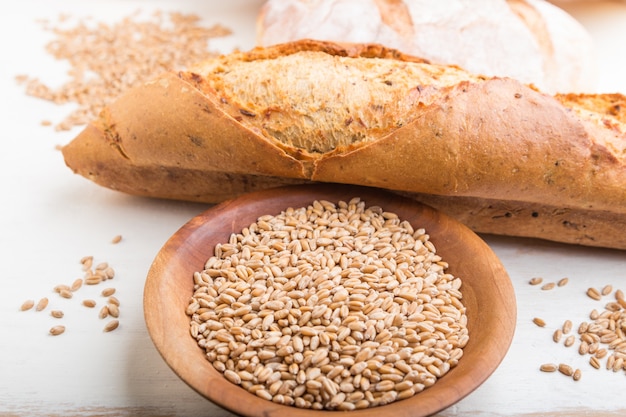 Pain frais et assiette en bois avec des graines de blé sur fond de bois blanc