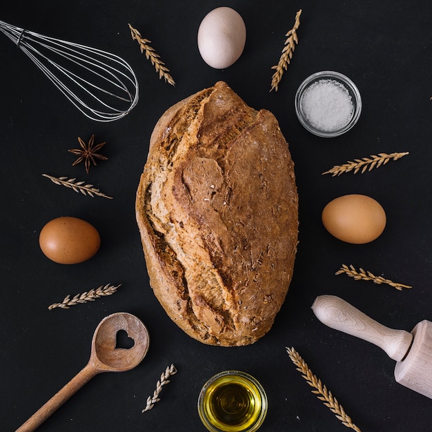 Pain frais entouré de divers ingrédients et ustensiles de cuisson sur fond noir