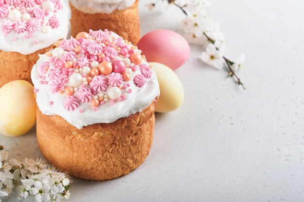 Pain ou gâteaux sucrés traditionnels de Pâques avec glaçage blanc et décor de sucre oeufs colorés et branche d'arbre de fleurs de cerisier sur tableau blanc Divers gâteaux de Pâques de printemps Joyeuses Pâques mise au point sélective