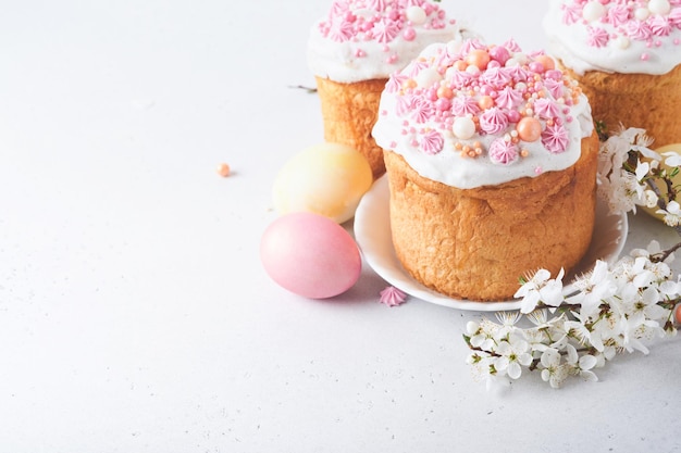 Pain ou gâteaux sucrés traditionnels de Pâques avec glaçage blanc et décor de sucre oeufs colorés et branche d'arbre de fleurs de cerisier sur tableau blanc Divers gâteaux de Pâques de printemps Joyeuses Pâques mise au point sélective