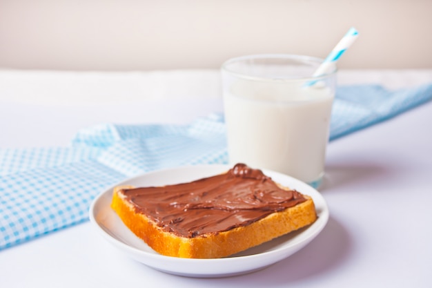 Pain grillé au beurre à la crème au chocolat, verre de lait sur la surface blanche