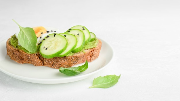 Pain grillé au concombre, œuf et basilic sur une assiette