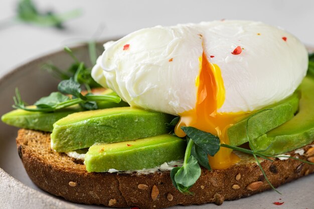 Pain grillé de blé entier avec avocat, œuf poché, pousses de pois et fromage