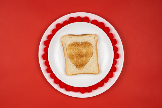 Pain grillé avec une brûlure en forme de cœur sur une table rouge. Concept de vacances de la Saint-Valentin. Petit déjeuner festif, déjeuner.