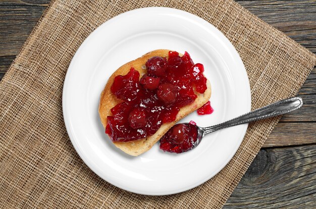 Pain grillé avec confiture de cerises dans une assiette sur fond de bois rustique, vue de dessus