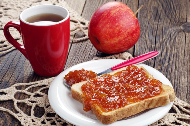 Pain grillé avec confiture et tasse de thé sur table en bois