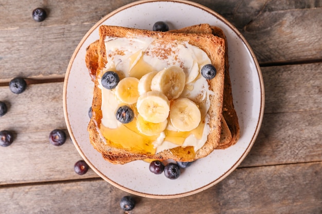 Pain grillé savoureux avec du miel, du beurre et des fruits sur une assiette