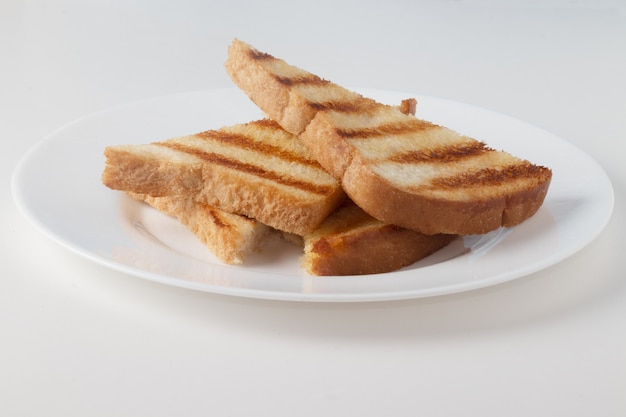 Pain de mie grillé avec du beurre sur une plaque blanche.