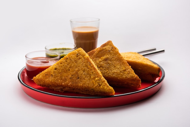Pain de mie Pakora ou pakoda en forme de triangle servi avec du ketchup aux tomates, chutney vert, collation indienne populaire à l'heure du thé